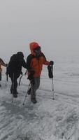 Mountaineering activity on the steep mountain slope. Clip. Group of extreme tourists walking one by one on icy surface of a hill in foggy cold weather. video