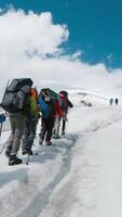 Climbers climb snowy mountain. Clip. Climbers follow each other in line to snowy peak on clear day. Group of climbers ascend snowy mountain on background of blue sky video