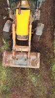 Top view of excavator working in field. Clip. Bulldozer clears plot of land with green thickets. Bulldozer clears a field of green grass video