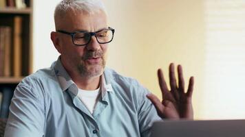 A senior man communicates via chat in a well-lit room filled with bookshelves and a warm atmosphere. video