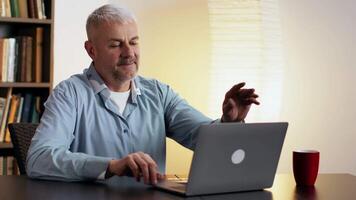 A man engages in a call while seated at a table, dressed comfortably, with a warm, inviting background. video