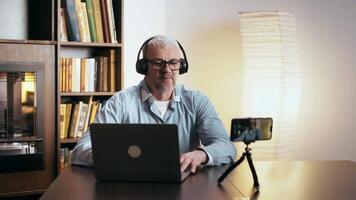 A man wearing headphones actively participates in a call while seated at a desk surrounded by bookshelves. video