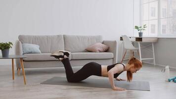 A woman in athletic wear performs push-ups on a yoga mat in her stylish living room. The space includes a sofa, plants, and bright natural light from the window. video
