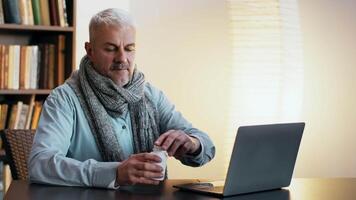 Sick Older man sitting at a table with a laptop and a bottle of supplements in a cozy indoor setting during the daytime video