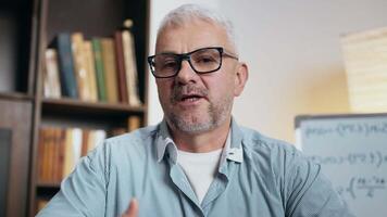 A man is animatedly discussing a topic in a study filled with books, gesturing expressively while seated at a desk. video