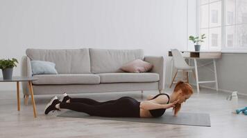 A woman is engaged in floor exercises on a mat in her stylish living room, surrounded by plants and furniture, focusing on her fitness routine and improving strength. video