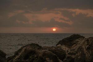 Sunset Ocean Rocks - Orange sunset over ocean viewed from rocky coastline. photo