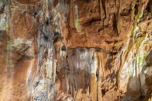 A rock wall with a lot of moss and some green spots. The wall is brown and has a lot of texture. photo
