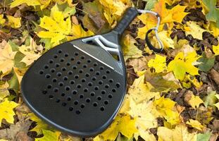 Top view of a black padel racket on a green court grass turf behind the net outdoors. Paddle is a racquet game. Professional sport concept with space for text photo