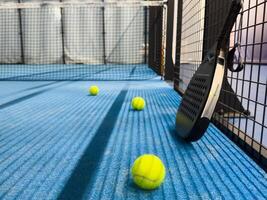 Padel racket and yellow ball behind net on a green court grass turf outdoors at sunset. Paddle is a racquet game. Professional sport concept with space for text photo