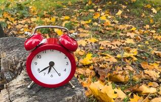 Traditional alarm clock on a background of orange and yellow maple leaves, fall time change concept photo
