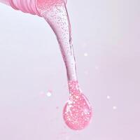 Shimmery Pink Gel Droplet with Glitter. A close-up of a shimmery pink gel droplet pouring with glitter, highlighting a luminous and hydrating texture against a soft background. photo