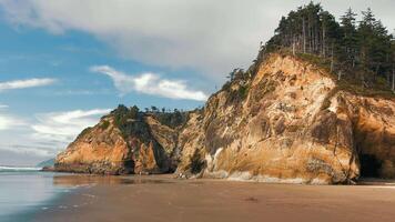 Cannon Beach Rugged cliffs and sandy shore with visitors. Large rugged cliffs dominate this sandy shore, where visitors explore the beach below. video