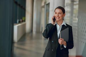 A professional woman in office is talking on phone while holding a folder and smiling photo