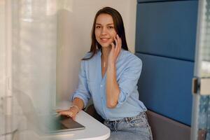 A smiling woman is having a phone call while working on a laptop in a modern office space photo