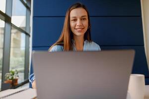 In a modern office setting, a woman with a smile is seen using a laptop for work photo