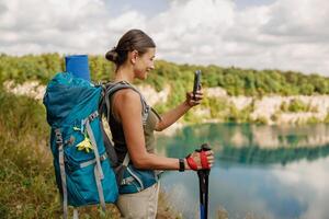 A Hiker is Enjoying a Relaxing Break at a Scenic Lake While Using a Smartphone to Capture the Moment photo