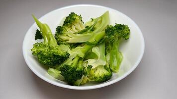 Cooked broccoli in a white bowl on a grey background, close up photo