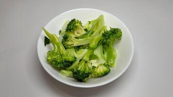 Cooked broccoli in a white bowl on a grey background, close up photo