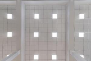cassette stretched or suspended ceiling with square halogen spots lamps and drywall construction in empty room in house or office. Looking up view photo