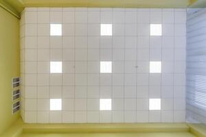 cassette stretched or suspended ceiling with square halogen spots lamps and drywall construction in empty room in house or office. Looking up view photo