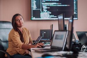 A businesswoman sitting in a programmer's office surrounded by computers, showing her expertise and dedication to technology. photo