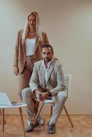 A business couple posing for a photograph together against a beige backdrop, capturing their professional partnership and creating a timeless image of unity and success. photo