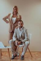 A business couple posing for a photograph together against a beige backdrop, capturing their professional partnership and creating a timeless image of unity and success. photo