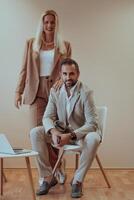 A business couple posing for a photograph together against a beige backdrop, capturing their professional partnership and creating a timeless image of unity and success. photo