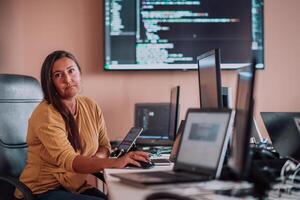A businesswoman sitting in a programmer's office surrounded by computers, showing her expertise and dedication to technology. photo