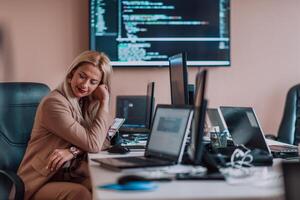 A businesswoman sitting in a programmer's office surrounded by computers, showing her expertise and dedication to technology. photo