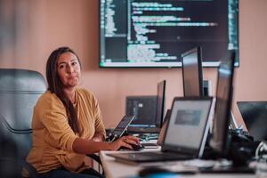 A businesswoman sitting in a programmer's office surrounded by computers, showing her expertise and dedication to technology. photo