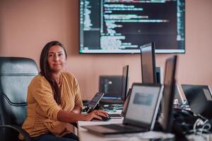 A businesswoman sitting in a programmer's office surrounded by computers, showing her expertise and dedication to technology. photo