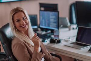 A businesswoman sitting in a programmer's office surrounded by computers, showing her expertise and dedication to technology. photo