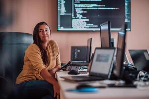 A businesswoman sitting in a programmer's office surrounded by computers, showing her expertise and dedication to technology. photo