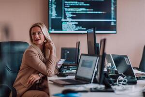 A businesswoman sitting in a programmer's office surrounded by computers, showing her expertise and dedication to technology. photo