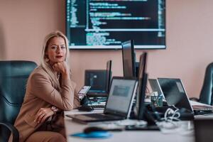 A businesswoman sitting in a programmer's office surrounded by computers, showing her expertise and dedication to technology. photo