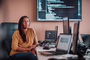 A businesswoman sitting in a programmer's office surrounded by computers, showing her expertise and dedication to technology. photo