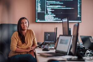 A businesswoman sitting in a programmer's office surrounded by computers, showing her expertise and dedication to technology. photo