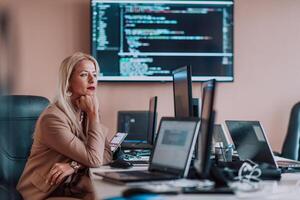 A businesswoman sitting in a programmer's office surrounded by computers, showing her expertise and dedication to technology. photo