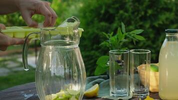 Making homemade lemonade outdoors, refreshing summer citrus drink. Hands adding ice cubes to pitcher. video