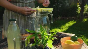 Summer vibes. Making homemade lemonade, refreshing summer drink in summer garden. Woman adds ice cubes to pitcher. video