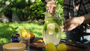Making homemade lemonade, refreshing summer drink. Hand stirs sugar with spoon in jug of lemonade. Cooking al fresco concept. video