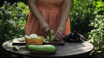 Person is slicing raw zucchini on cutting board outside during summer. Meal preparation. video