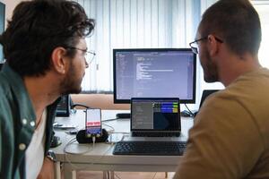 Programmers engrossed in deep collaboration, diligently working together to solve complex problems and develop innovative mobile applications with seamless functionality. photo