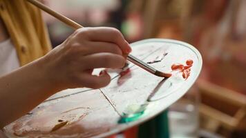 In an art studio, artist mixes a watercolor paints on a palette to create a rustic masterpiece on canvas. Woman painting with tools and showing her skill, artwork creation. Close up. Camera A. video