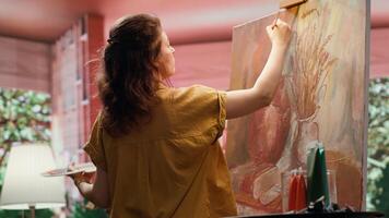 In a rustic workshop, artist mixes a variety of watercolor paint on palette to create a colorful masterpiece on canvas. Woman painting with a brush and showing her skill, artwork creation. Camera A. video