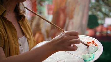 In an art studio, artist mixes a watercolor paints on a palette to create a rustic masterpiece on canvas. Woman painting with tools and showing her skill, artwork creation. Close up. Camera B. video