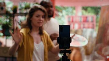 Woman artist hosting online class to present products and technique used on rustic artwork, recording tutorial online. Team of painters doing master class for e learning, art instruction. Camera A. video