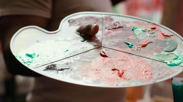 In an art studio, painter mixes multiple watercolor paints on a palette to create artwork on canvas. Skilled man painting with tools and showing imagination, artistic creation. Close up. Camera A. video